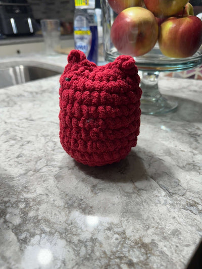 Red crocheted owl figure sitting on a marble countertop with apples in the background.